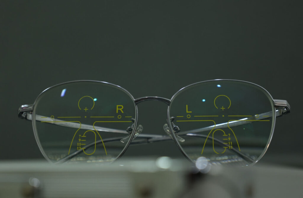 A pair of progressive eyeglasses sit on a table. They are been marked to show the different visual fields on each lens.