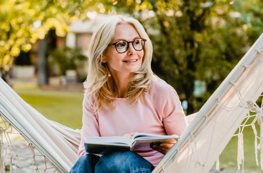 A person sitting in a hammock reading a book while wearing progressive glasses looks off into the distance.