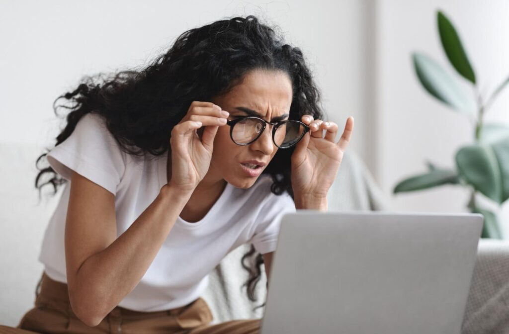 A person at work adjusting their glasses and squinting at their computer in frustration due to poor vision.