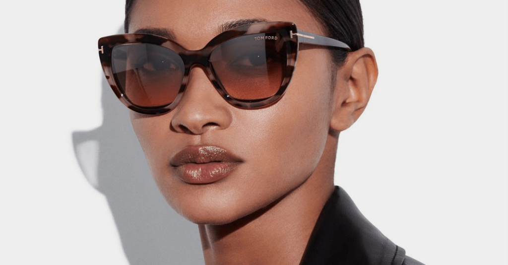 A close-up of a model wearing Tom Ford cat-eye sunglasses with a dark tortoiseshell frame and brown gradient lenses.