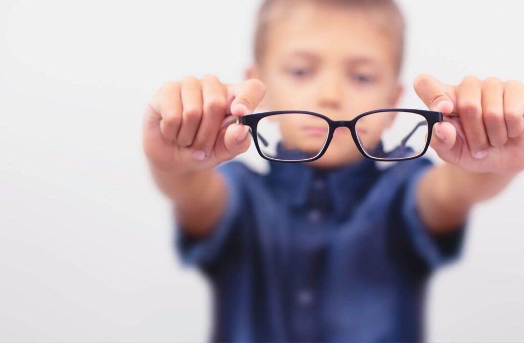 A blurry child holds up a pair of glasses into focus.