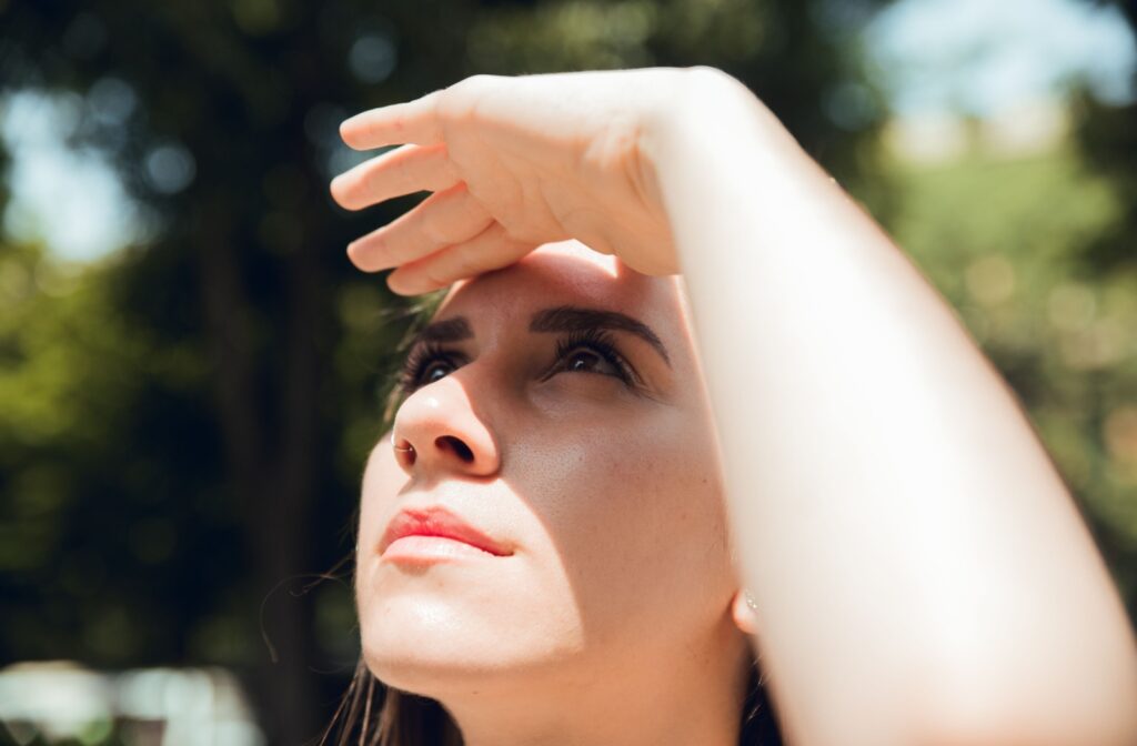 A person shielding thier eyes from the sun without wearing proper sun protection on their eyes.