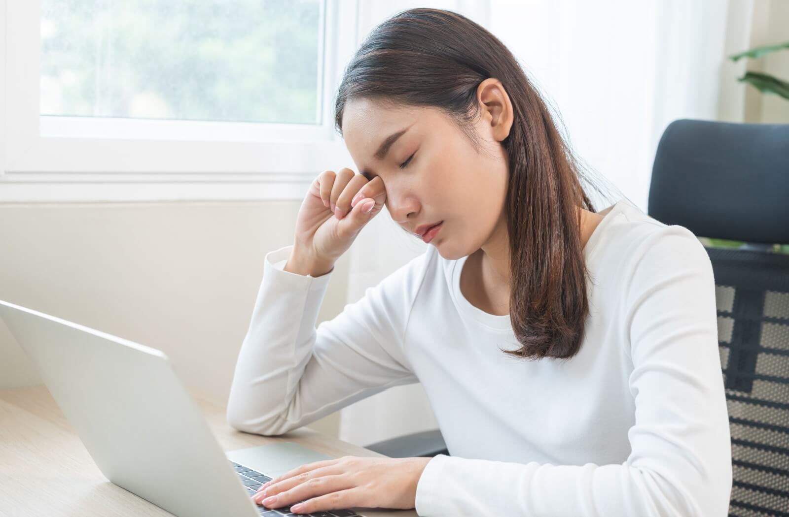 Person experiencing eye discomfort at a computer.