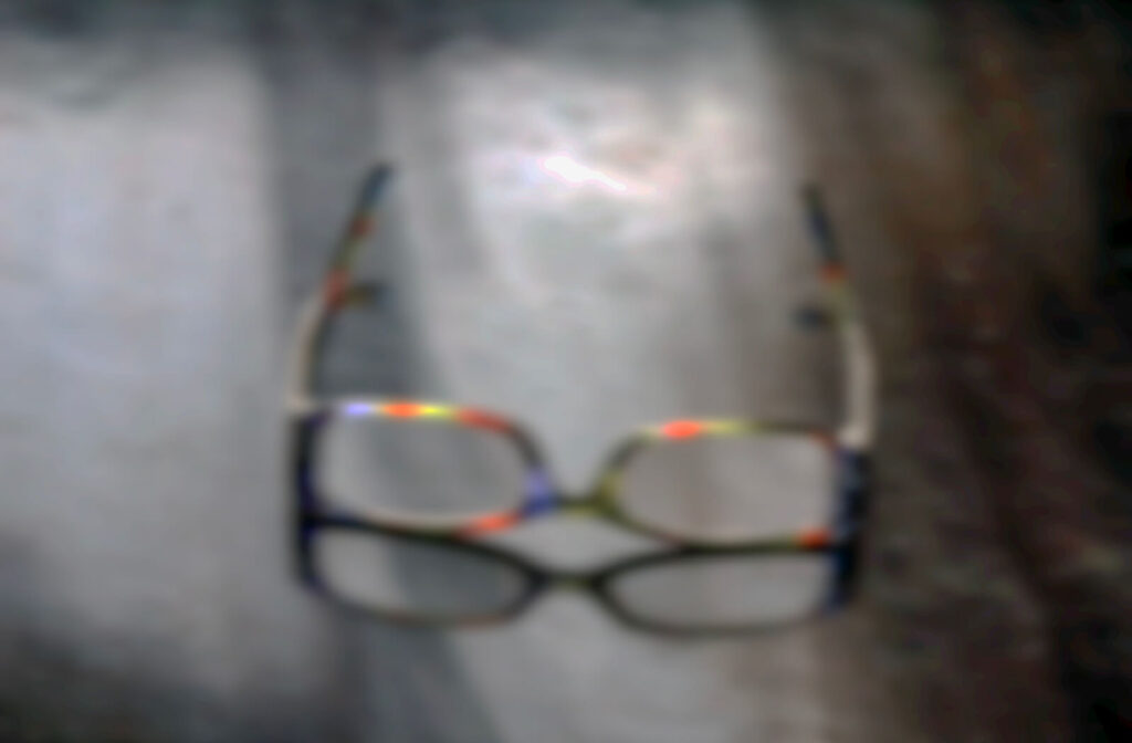 A blurry first-person view of a pair of colorful eyeglasses on a table, illustrating how dry eyes can cause significant vision blurriness.